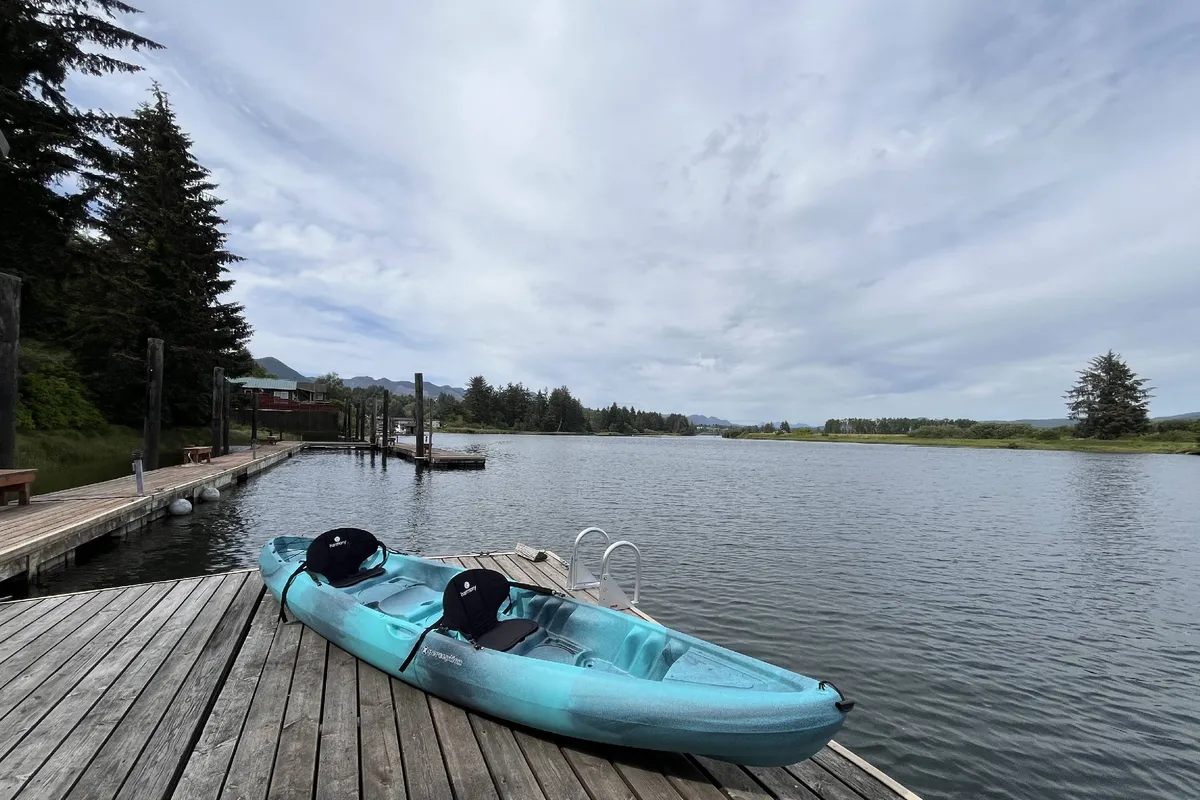 A wide-angle view of the dock area shows a kayak perched and ready for use, with lush trees surrounding the water’s edge. The perspective highlights both the readiness for adventure—kayaking, fishing, or exploring—and the serene, private feel of the property’s outdoor area.