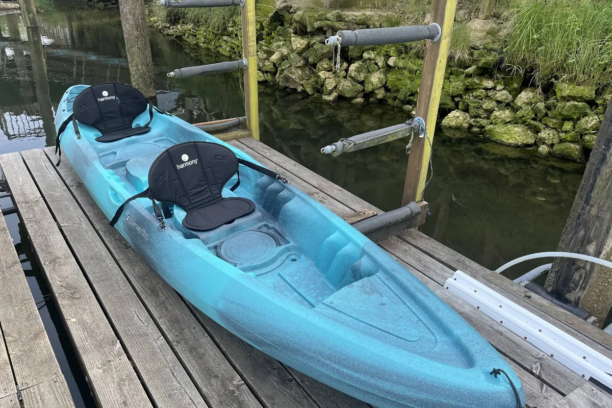 This image captures a kayak resting on a private dock, with the shimmering water surface stretching out beyond. The scene is bright and inviting, immediately highlighting the direct river access and the promise of adventure or relaxation on the water. The composition puts the viewer in the position of stepping onto the dock, ready for a paddle or to simply enjoy the tranquil setting.