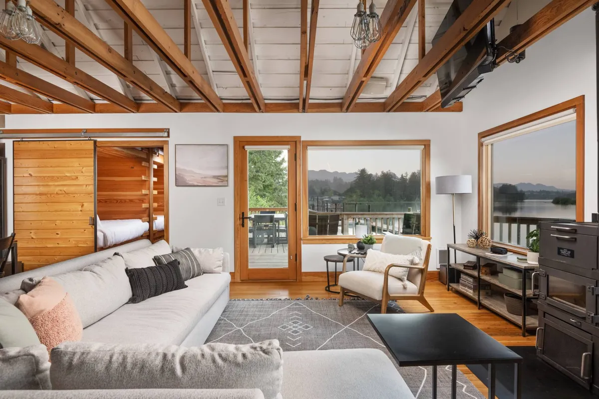A welcoming living area featuring a comfortable sectional sofa oriented toward large windows with panoramic views, wooden beams on the ceiling, and a tranquil, well-lit ambiance. The arrangement highlights the relaxing atmosphere and the scenic outlook, ideal for unwinding alone or with friends and pets.