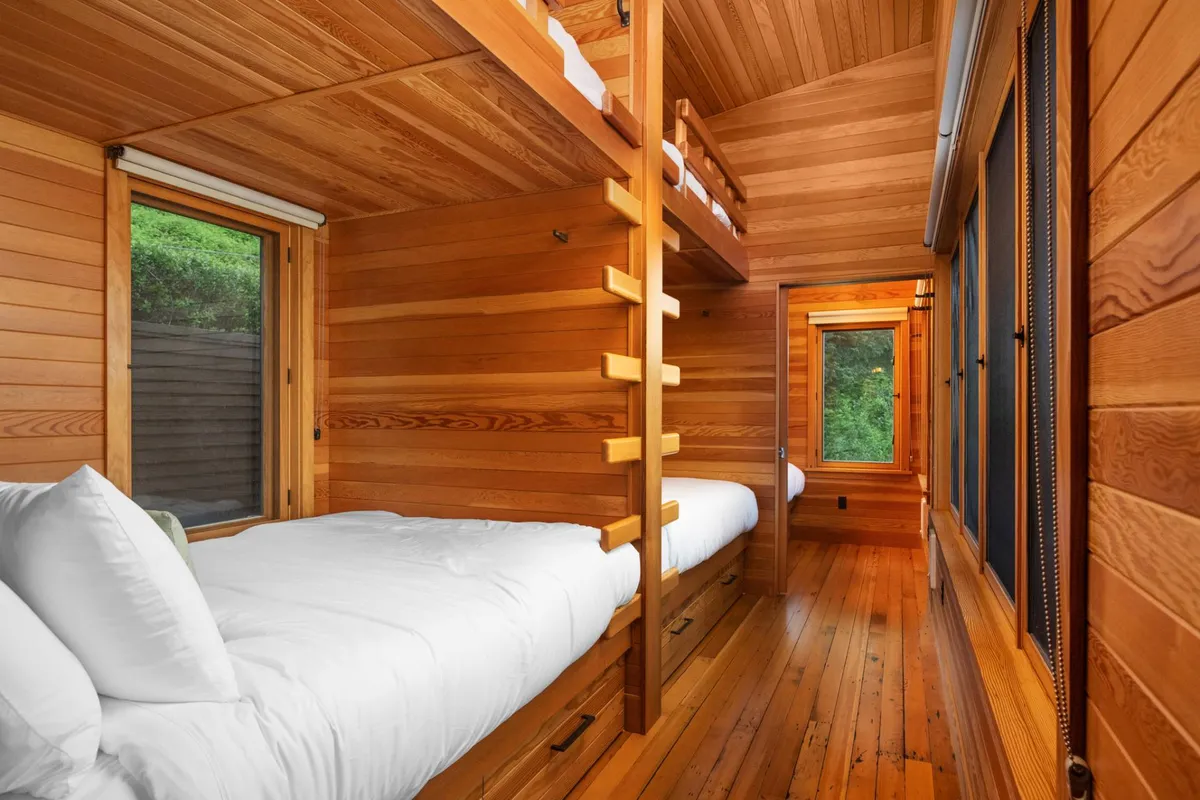 A cozy bedroom with queen-over-queen bunk beds, large windows letting in natural light, and rich wooden finishes. The space looks inviting and designed for multiple sleepers, ideal for families or groups.